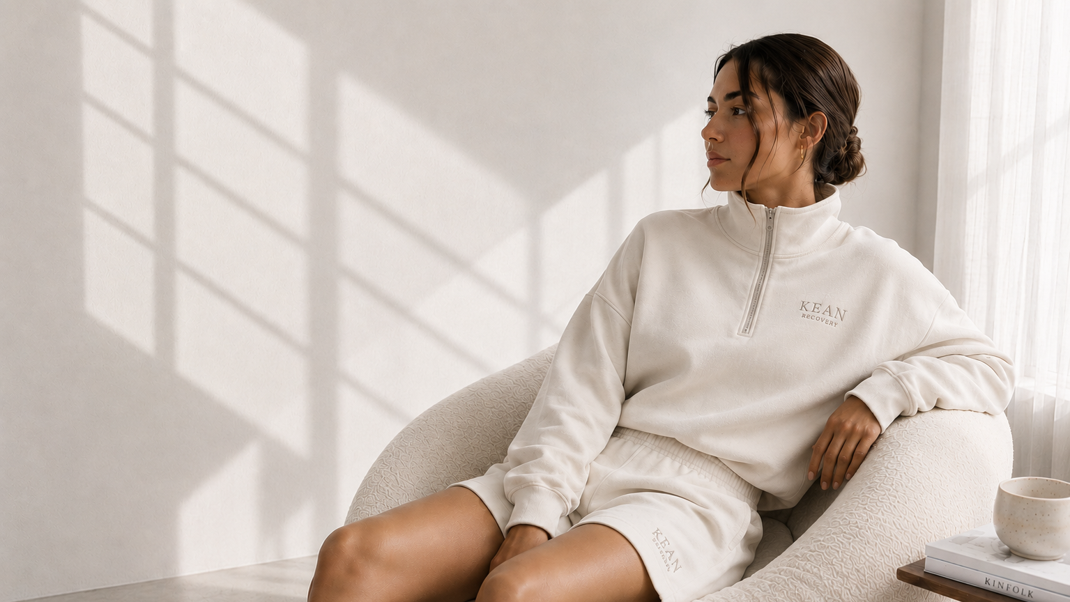 Woman wearing a white sweatshirt sitting on a chair in a bright room.